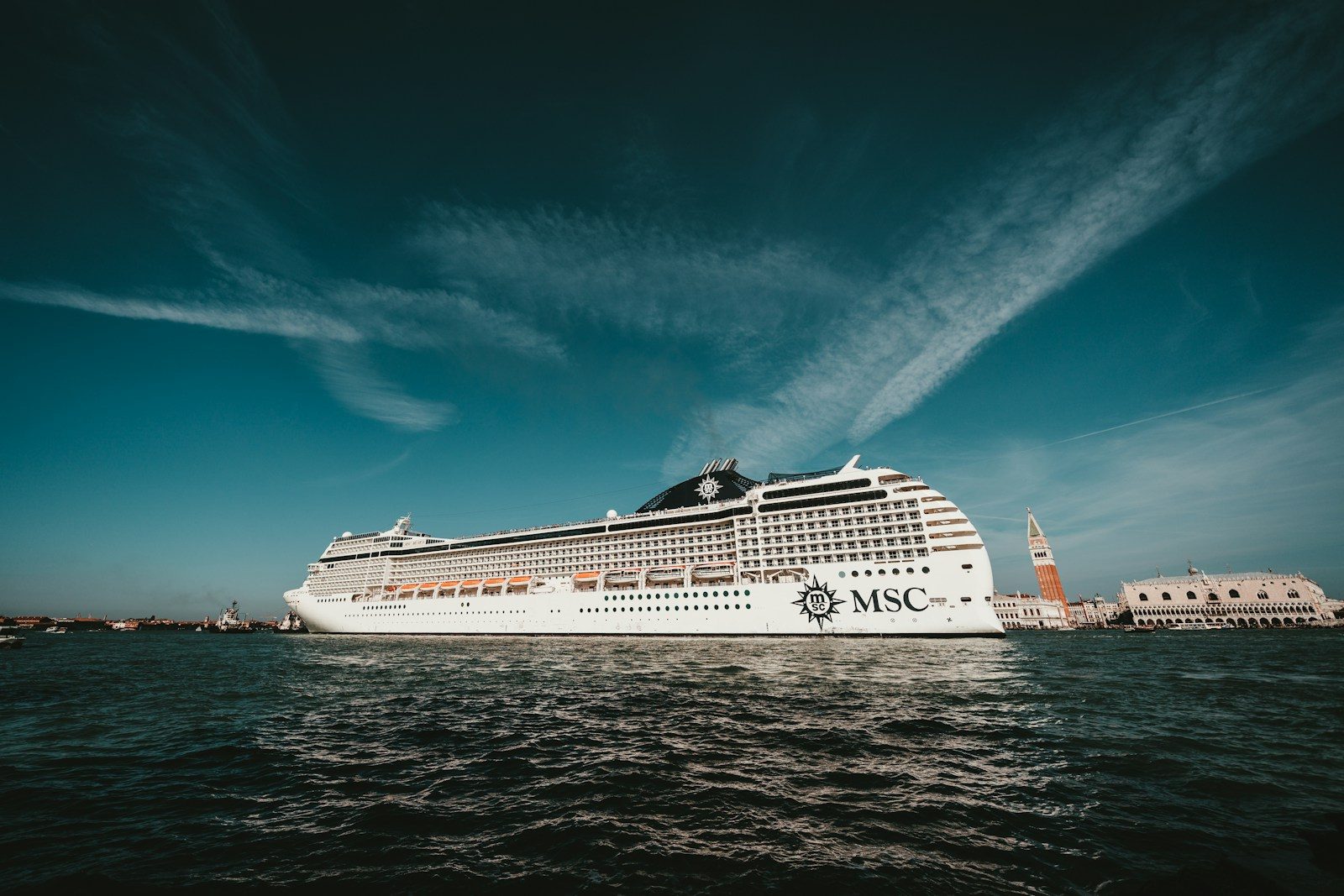 MSC cruise ship with the MSC logo on its hull sailing past St Mark's Campanile and the Doge's Palace in Venice, Italy